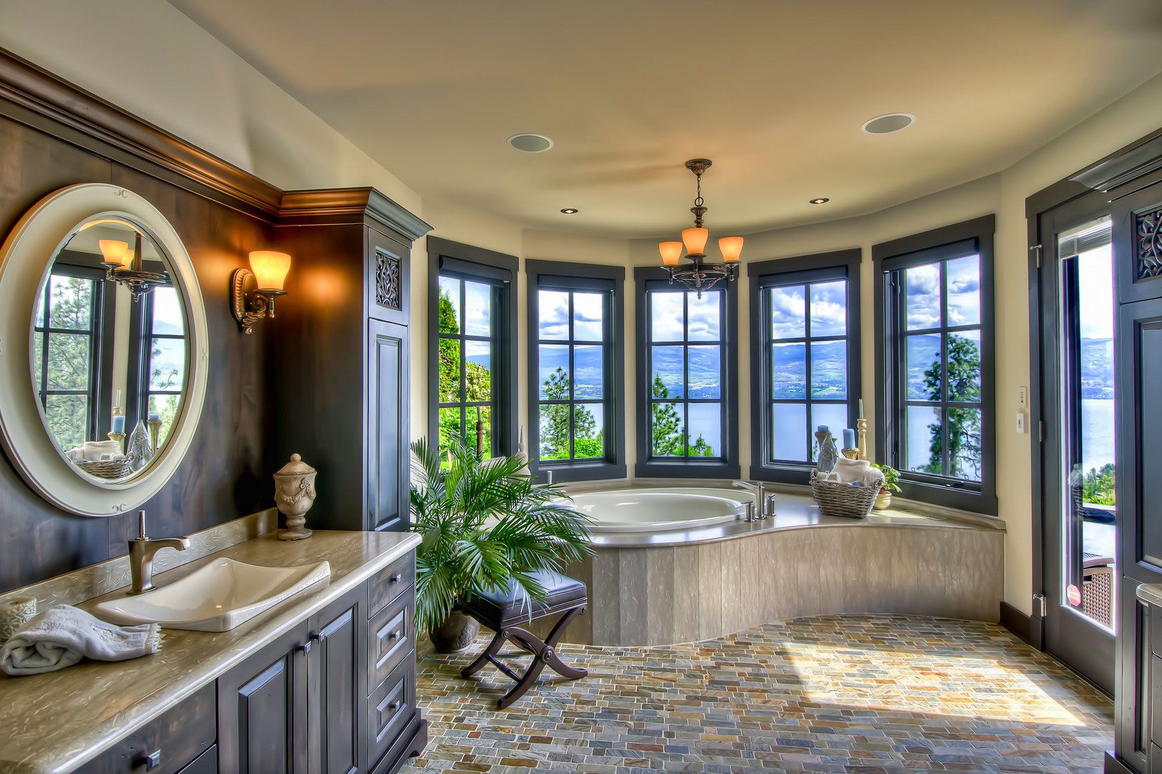 A round bathroom with a stone tub deck and windows facing the lake