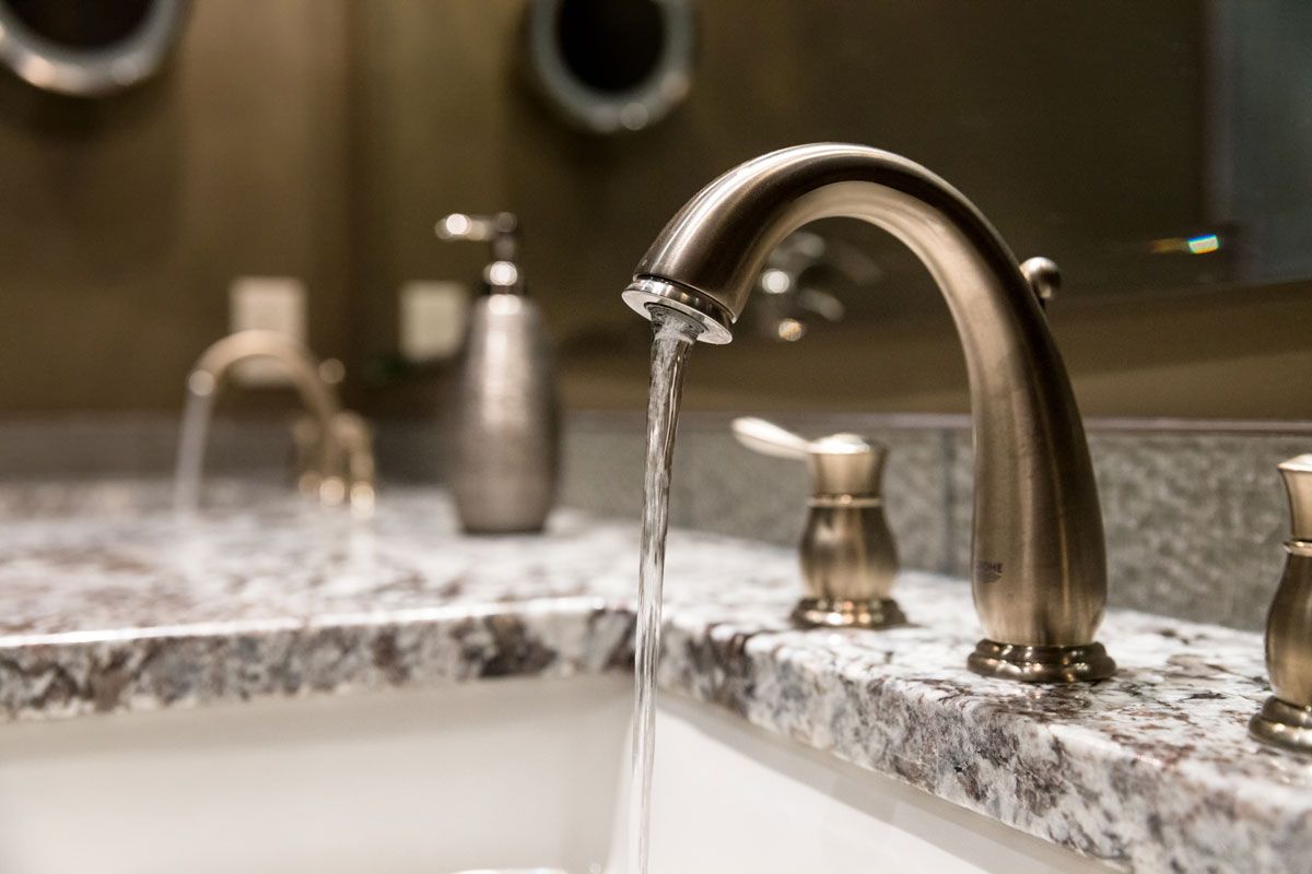 Close-up of a polished granite vanity edge with a running faucet